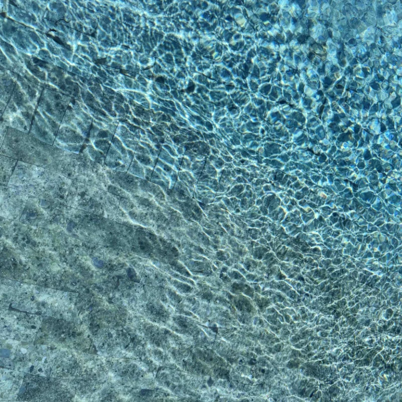 overhead view of crystal-clear pool water rippling over Bali green natural stone tiles.
