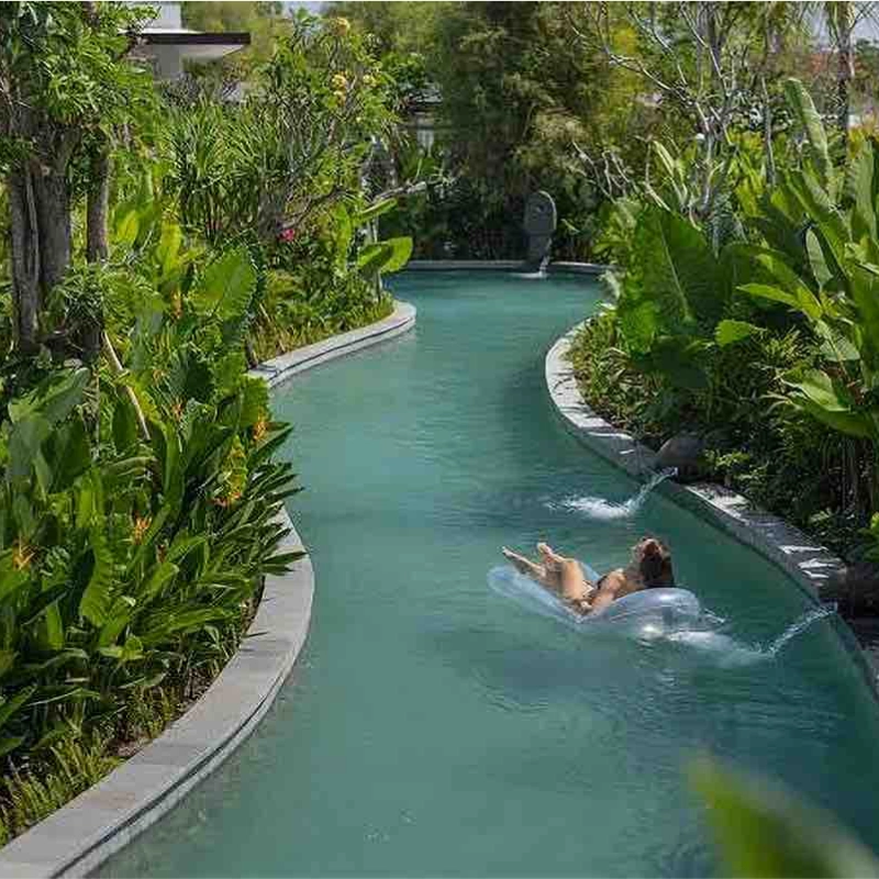 This image features a long, meandering lazy-river style pool lined with Bali Green natural stone tiles