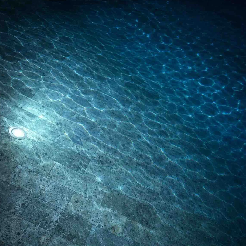 This image shows Bali Green Stone swimming pool tiles submerged night time beneath clear water, creating a beautiful blend of natural green-grey stone and deep blue-green water.